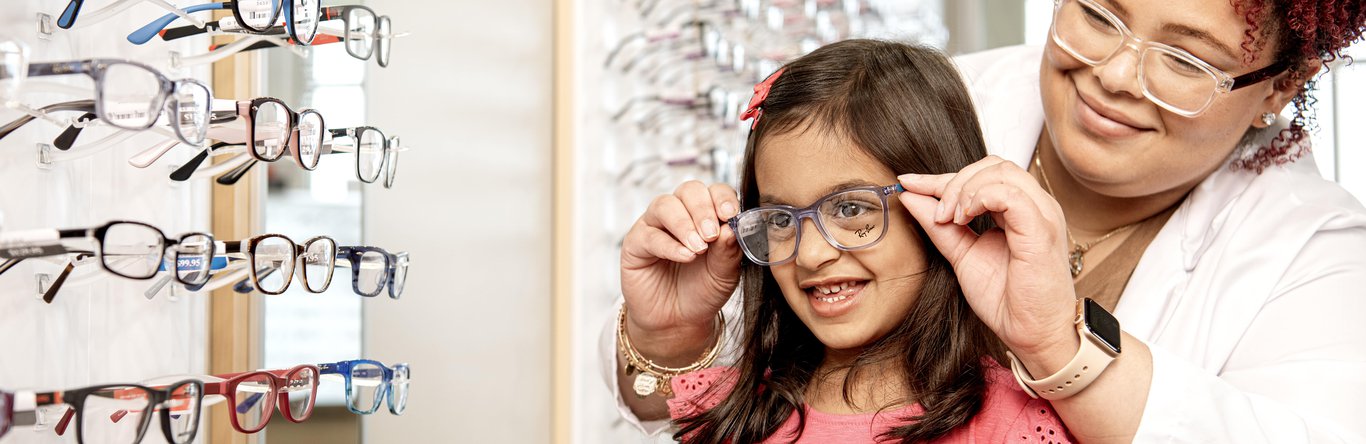 Women helping young girl try on glasses