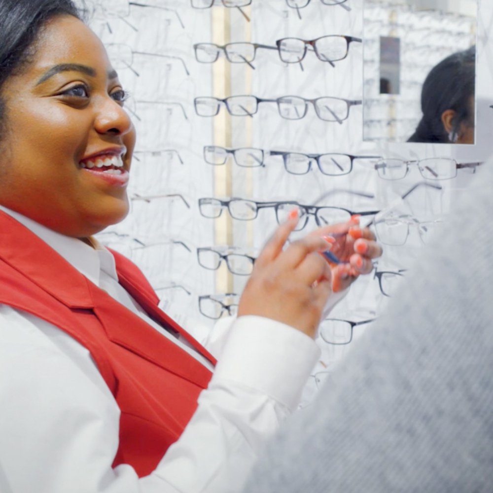 Smiling female African American National Vision employee helping a customer pick out new frames.