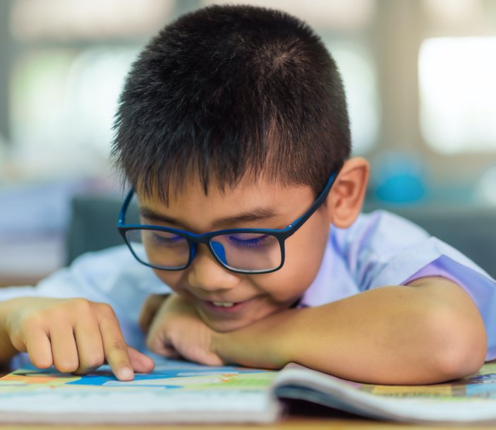Young boy wearing glasses and reading a book.