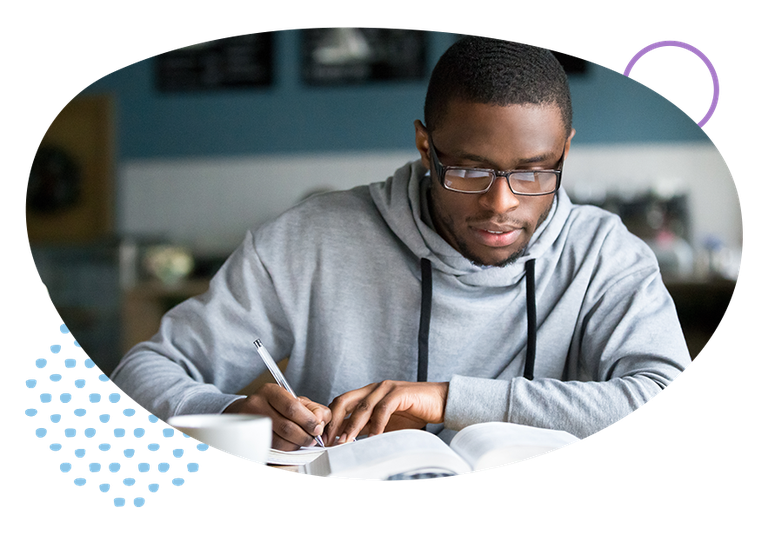 Young man wearing glasses looking at a book and writing